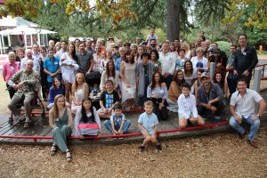 A large group of people stand under a tree, all there to celebrate Cherry Parker's 90th birthday. Cherry stands in the middle of them all.
