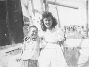 Two young Japanese people grin at the camera. The young boy is Charlie, around 12 years old. The young woman is Nobuko Sakuramoto, also known as Cherry Parker, who has her arm around Charlie and is around 18 years old.